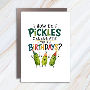 以下が含まれることがあります： 「HOW DO PICKLES CELEBRATE THEIR BIRTHDAYS?」というカラフルな文字が書かれた白いグリーティングカード。文字の下には、それぞれ異なる柄のパーティーハットをかぶり、手足が生えた3本の緑色のピクルスのイラストが描かれています。