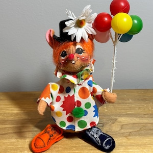 May include: A whimsical clown doll with orange fur, a black top hat, and a daisy. The doll wears a colorful polka-dot shirt and holds a bunch of balloons. The clown has orange and navy blue shoes. A vintage-style collectible.