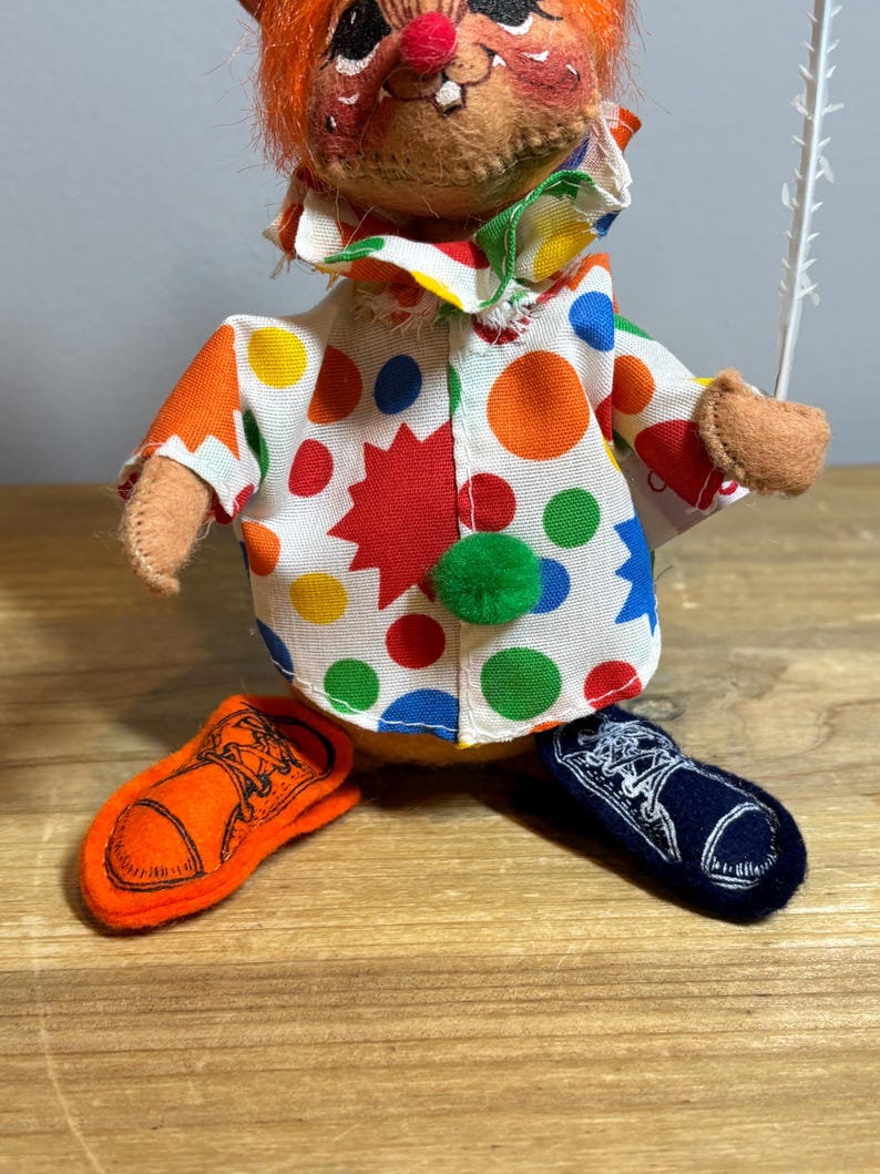 May include: A vintage clown doll with orange hair, a red nose, and a colorful polka-dot outfit. The doll has orange and navy blue shoes. The clown's outfit features a white shirt with large red, yellow, green, and blue polka dots.