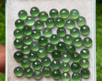 Op de afbeelding: Een verzameling gefacetteerde, ronde, groene edelstenen, weergegeven in een witte tray. De edelstenen hebben een gepolijst, reflecterend oppervlak en zijn dicht op elkaar geplaatst. De kleur is een levendig, doorschijnend groen.