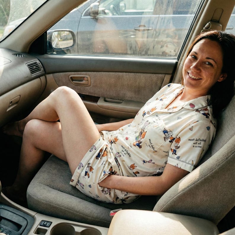 May include: A person wearing a cream-colored pajama set with a cartoon fox and bunny print, sitting in the front seat of a car. The pajama set includes a short-sleeved top and shorts.