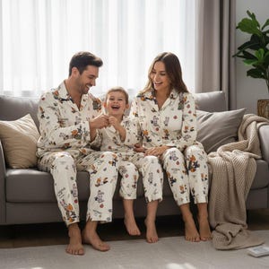 May include: Matching family pajama sets in cream with a cartoon animal print. The sets include button-down shirts and pants. A family of three is sitting on a gray couch, all wearing the pajamas and smiling.