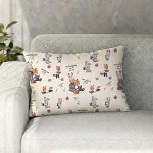 May include: Rectangular pillow with a repeating pattern of cartoon foxes and rabbits reading books, with apples and pencils scattered across a cream background. The text "most definitely not all in a row" is also present.