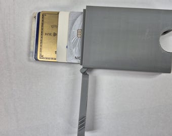 May include: A grey card holder with a pull-out lever, containing several credit cards. The cards are visible, showing various colours and designs. The holder is made of a solid, possibly metallic material.