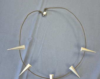 May include: A silver-colored necklace with five triangular pendants evenly spaced along a black cord. The necklace is displayed on a blue surface. The pendants are pointed and metallic.