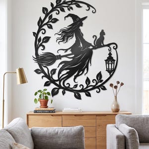 May include: A black metal wall art piece shaped like a crescent moon, featuring a silhouette of a witch with long hair wearing a pointed hat, riding a broomstick with a cat sitting behind her and a hanging lantern suspended from the broom handle.