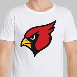 May include: White t-shirt featuring a stylized red cardinal head with a yellow beak and black accents. The cardinal graphic is centered on the chest. The shirt has a crew neck and short sleeves.
