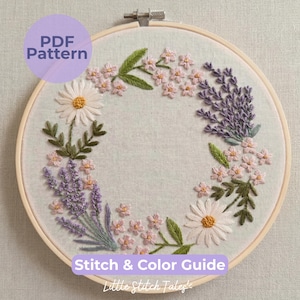 Può includere: Un telaio da ricamo circolare in legno contenente un motivo a corona floreale su tessuto chiaro. Il design presenta margherite bianche con centri gialli, rametti di lavanda viola e piccoli fiori rosa con foglie verdi. Il testo recita PDF Pattern.