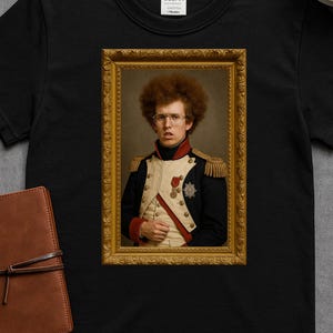 May include: Black t-shirt featuring a framed portrait of a person with curly red hair and glasses, dressed in a military-style uniform. The portrait is in a gold ornate frame. The shirt has a Gildan tag.