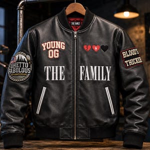 May include: A black leather bomber jacket featuring a front zip, ribbed cuffs, and collar. Patches include 'YOUNG OG', three heart icons, and 'GHETTO FABULOUS'. The text 'THE FAMILY' is embroidered on the chest, with 'BLOOD'S THICKER' on the sleeve.