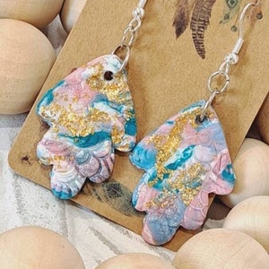 May include: A pair of dangle earrings with a pink, blue and gold abstract design. The earrings are made of polymer clay and have silver hooks.