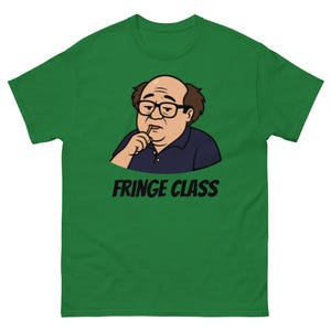 Puede incluir: Camiseta verde con una ilustración de dibujos animados de un hombre con gafas y el texto "FRINGE CLASS" en negro. El hombre tiene cabello castaño y una camisa azul oscuro, sosteniendo un palillo.
