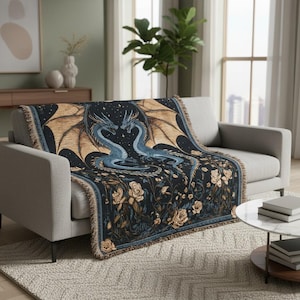 Può includere: Una coperta nera con un design di drago fantasy. Due draghi blu si fronteggiano, formando un cuore. La coperta ha ali color cuoio, rose color crema e un bordo con frange. La coperta è drappeggiata su un divano grigio.