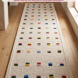 Puede incluir: Una alfombra rectangular de color crema con un patrón repetitivo de pequeños cuadrados multicolores en rojo, azul, amarillo, verde y rosa. La alfombra mide 2,5 pies de ancho. El texto en la imagen ofrece detalles sobre variaciones de ancho.