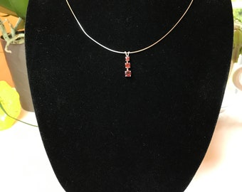 May include: A silver chain necklace with a pendant featuring three small, red, square-shaped gemstones.
