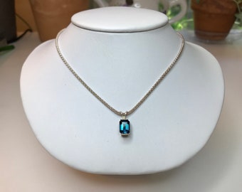 May include: A silver necklace with a rectangular, deep blue pendant. The pendant is set in a silver bezel and hangs from a delicate chain. The necklace is displayed on a white bust.
