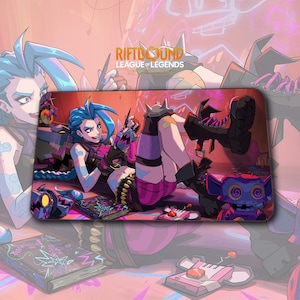 May include: A rectangular mousepad featuring a colorful illustration of a female character with blue hair from the League of Legends game. The character is wearing a pink and black outfit and is surrounded by other game-related elements.