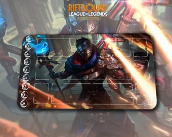 May include: A rectangular Riftbound League of Legends Trading Card Game playmat. The mat features a warrior character with a blue and red scarf, holding a staff with a blue orb. The mat has numbered zones and the game's logo.