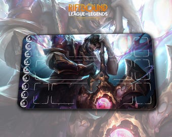 May include: A rectangular playmat featuring a detailed illustration of a character from League of Legends. The mat has a dark background with a central image of a warrior and a glowing orb. The text "RIFTBOUND LEAGUE OF LEGENDS" is visible.