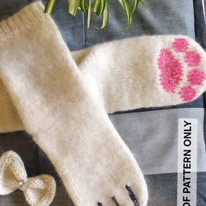 May include: A pair of off-white knitted socks with a pink paw print design on the toes and black claw details. A small, white bow with a rhinestone center is also visible. The text "PDF PATTERN ONLY" is in the image.