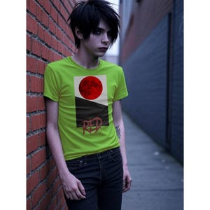 以下が含まれることがあります： ライムグリーンのTシャツ。赤い円、黒い部分、そして「RED」の文字が描かれたグラフィックデザイン。Tシャツは黒いジーンズと合わせて着用されています。