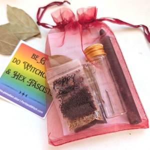 May include: A red organza drawstring bag containing a small clear plastic bag labeled Poppy Seeds, a clear glass vial with a gold cap, and a dark brown stick. A square card with a rainbow gradient reads BE GAY DO WITCHCRAFT & HEX FASCISTS.