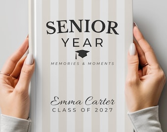 以下が含まれることがあります： ストライプのベージュと白の表紙が付いたハードカバーの思い出の本。「SENIOR YEAR」は「MEMORIES & MOMENTS」と「Emma Carter CLASS OF 2027」の上に表示されています。卒業帽のグラフィックも含まれています。