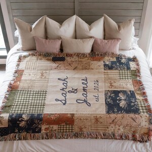 May include: A woven throw blanket featuring a patchwork design with various patterns including floral, gingham, and swan motifs in shades of blue, green, and tan. The center panel displays the text Sarah & James est. 2026 in dark blue script.