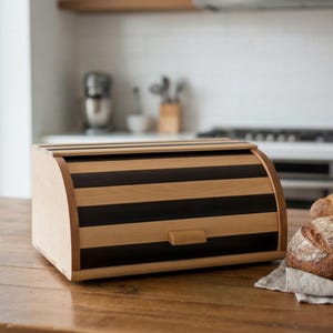 Op de afbeelding: Een houten brooddoos met een roldeksel. De doos heeft afwisselende horizontale strepen van licht en donker hout. Een klein houten handvat zit aan de voorkant. De brooddoos staat op een houten tafel in een keuken.