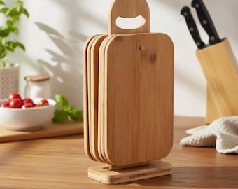 May include: A set of bamboo cutting boards with a handle and a stand. The boards are rectangular with rounded corners and are stacked together. The stand is also made of bamboo and has a rectangular base. A knife block and a bowl of tomatoes are in the background.