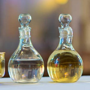 May include: Two clear glass bottles with stoppers, one filled with a clear liquid and the other with a yellow liquid. The bottles have a rounded base and a narrow neck, with a glass stopper on top.