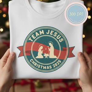 May include: White crew neck sweatshirt with a circular graphic. The graphic reads "TEAM JESUS CHRISTMAS 2025" and features a nativity scene illustration in teal, red, and white. A digital print quality sticker is in the upper right corner.