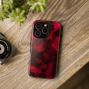 May include: A smartphone case with a vibrant red and black geometric pattern. The case has a glossy finish and is designed to fit a modern smartphone with multiple camera lenses. The case is resting on a wooden surface.