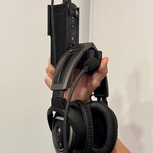 May include: Black Bose aviation headset with a microphone and a control unit. The headset has a silver-coloured band and black earcups. The control unit has the text "K320 AIRBUS".