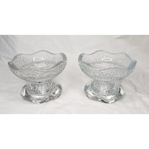 May include: Two clear glass dessert bowls with textured, wavy rims and pedestal bases. The bowls are made of clear glass and are designed for serving ice cream or other desserts. The bowls are displayed on a white surface.