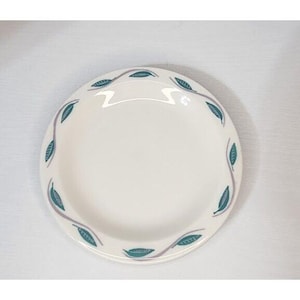 May include: White ceramic plate with a teal and purple leaf design around the rim. The plate has a simple, elegant design, suitable for everyday use or special occasions. The plate is round and has a slightly raised edge.