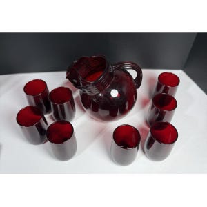 May include: A vintage ruby red glass pitcher and tumbler set. The pitcher has a handle and a spout. The set includes eight matching tumblers. The glassware is a deep red color, perfect for serving beverages.