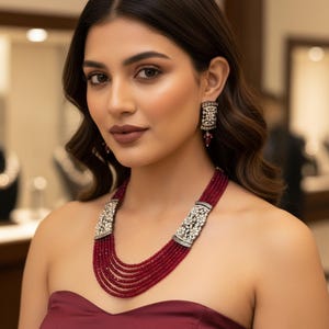 May include: A multi-strand ruby red necklace with ornate silver clasps and matching earrings. The jewelry set is worn with a burgundy strapless top. The earrings have a rectangular shape with a ruby red drop.
