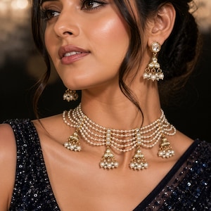 Peut inclure: Un ensemble élégant de collier et de boucles d'oreilles en perles. Le collier présente plusieurs rangées de perles avec des accents dorés et des grappes de perles pendantes. Les boucles d'oreilles reprennent le design avec une goutte de perle et d'or. La femme porte un haut bleu foncé à paillettes.