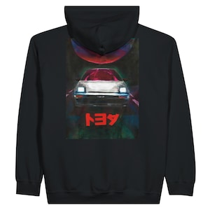 May include: Black hooded sweatshirt featuring a graphic of a car with red accents and Japanese text. The car is centered on the back of the sweatshirt, with a red sun-like shape above it. The design has a retro, artistic style.