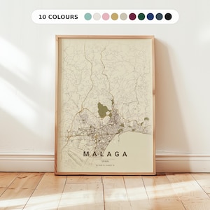 May include: A framed map print of Malaga, Spain, in neutral tones. The map features detailed street and terrain outlines, with the city name and coordinates at the bottom. The frame is light wood, and the print is displayed against a white wall.