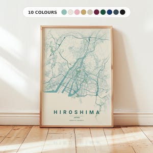 Puede incluir: Un mapa enmarcado de Hiroshima, Japón, en verde azulado y crema. El mapa muestra el diseño de la ciudad con calles y vías fluviales. El texto "HIROSHIMA JAPAN" está en la parte inferior, con coordenadas. El marco es marrón claro.