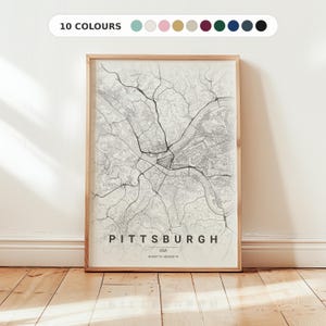 Op de afbeelding: Een ingelijste verticale wandkunstprint met een gedetailleerde zwart-wit stadsplattegrond van Pittsburgh, VS. De kaart toont complexe wegennetwerken en rivierpaden, met de tekst PITTSBURGH, USA en coördinaten onderaan in het midden gedrukt.