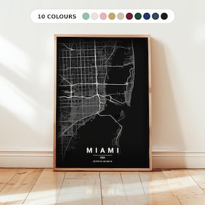 May include: A framed black and white map of Miami, USA, with the city's name and coordinates at the bottom. The map is displayed in a wooden frame, with a white background and a wooden floor.