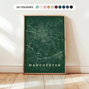 May include: A framed map print of Manchester, UK, in a dark green colour scheme. The city's road network is highlighted in white. The text "MANCHESTER" and "UK" are displayed at the bottom. The top of the frame shows "10 COLOURS".