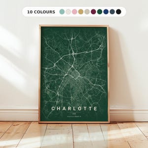 Op de afbeelding: Een rechthoekige wandkunstprint met een donkergroene kaart van Charlotte, USA, met witte lijnen die straten en snelwegen weergeven. De tekst luidt CHARLOTTE USA 35.2272 N / 80.8431 W. Een balk bovenaan toont 10 COLOURS met cirkelvormige kleurstalen.
