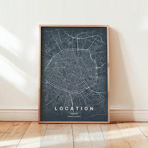 May include: A framed print showing a detailed map of a city, in shades of grey and white against a dark background. The word "LOCATION" is displayed in white text. The frame is a light wood colour.