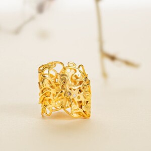 May include: A gold ring with a delicate, intricate design. The ring is made of a filigree pattern with small, clear stones.