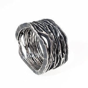 Puede incluir: Un anillo de plata con un diseño texturizado y en capas. El anillo está oxidado, lo que le da un aspecto oscuro y antiguo.