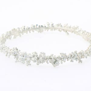 Könnte beinhalten: Ein silbernes Armreif-Armband mit einem zarten, organischen Design. Das Armband besteht aus kleinen, geclusterten Perlen, die ein strukturiertes, blütenartiges Muster erzeugen.